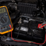 mechanic with black gloves diagnosing a weak car battery with multimeter