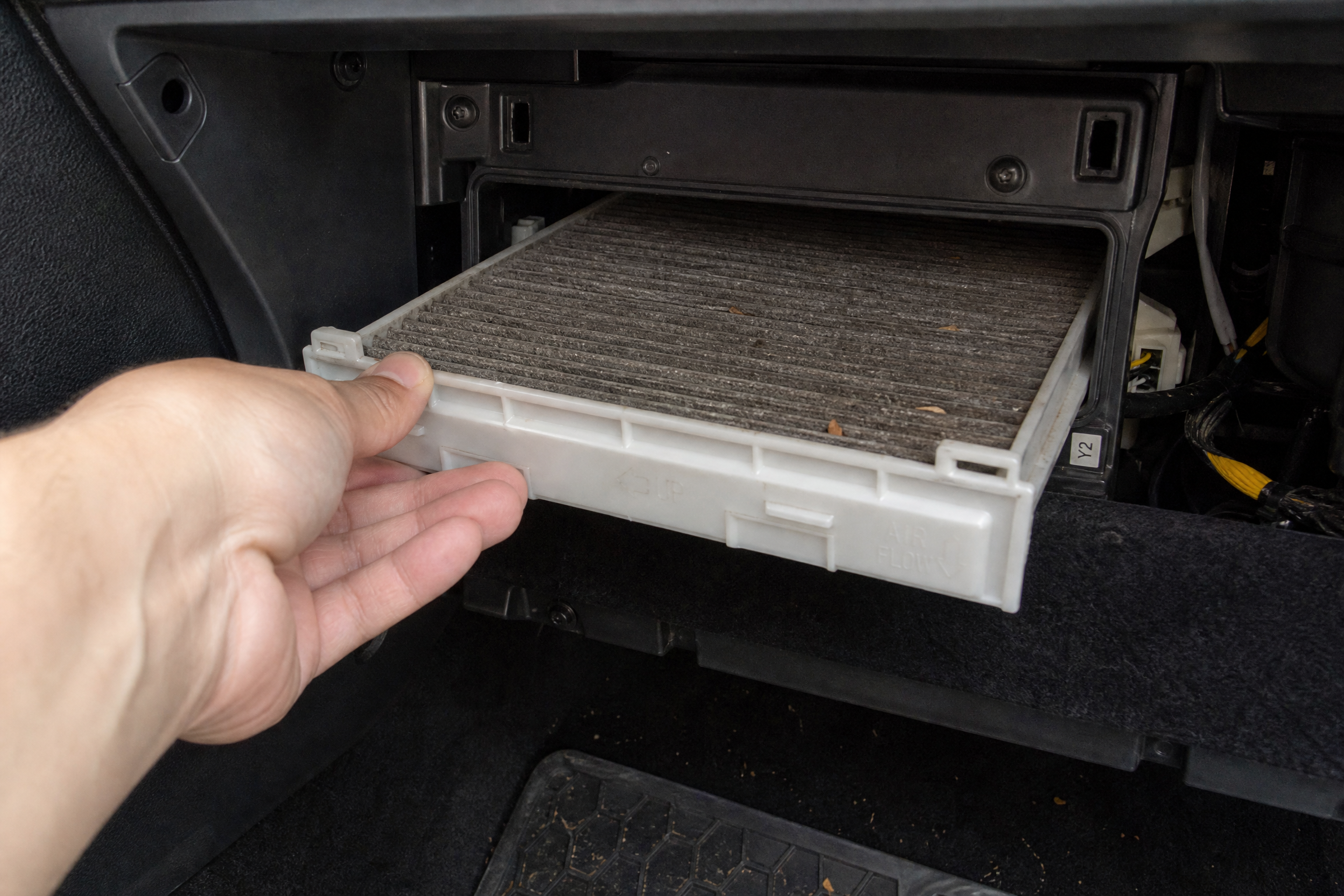 Diagram of a glovebox dropped open showing the cabin air filter housing behind it