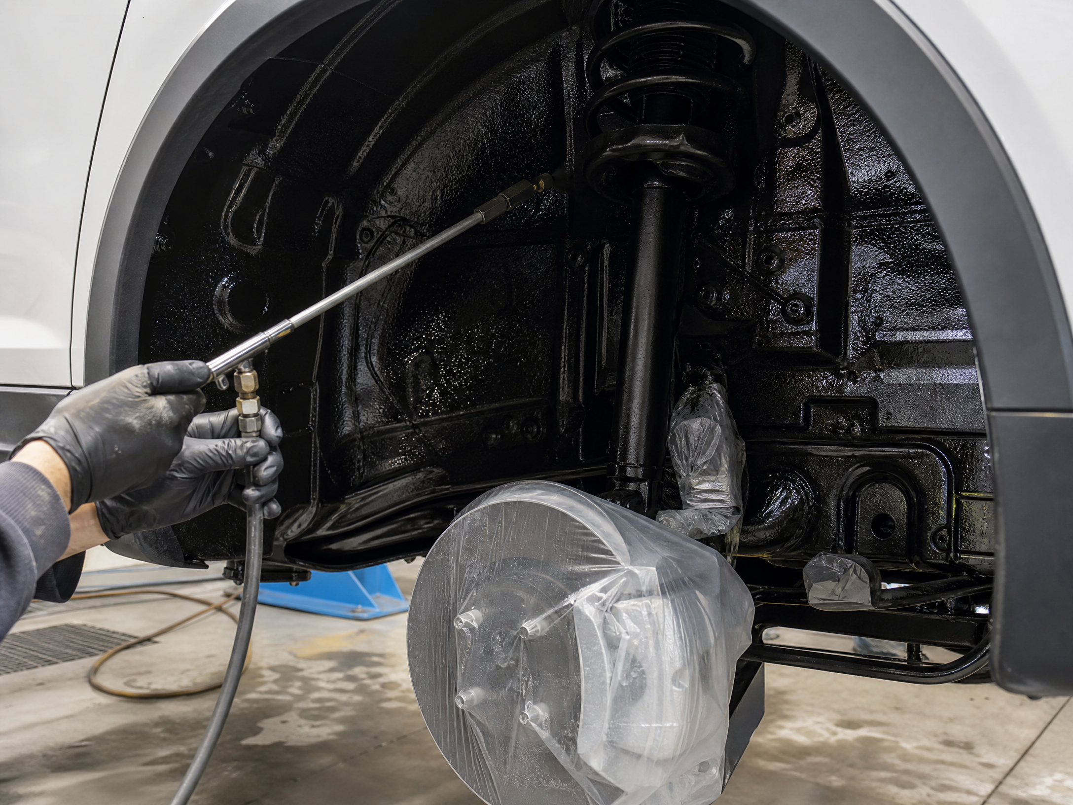 Technician applying rustproofing compound inside a wheel well